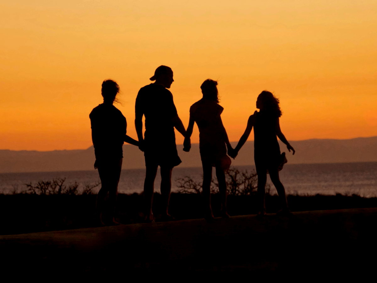 Vierköpfige Gruppe von Männern und Frauen halten sich die Hände im Sonnenuntergang