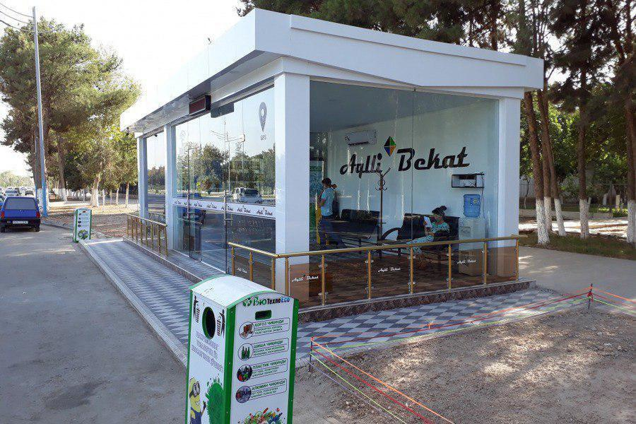 Modern glass bus stop with Cyrillic signage and a recycling bin in Tashkent, Uzbekistan