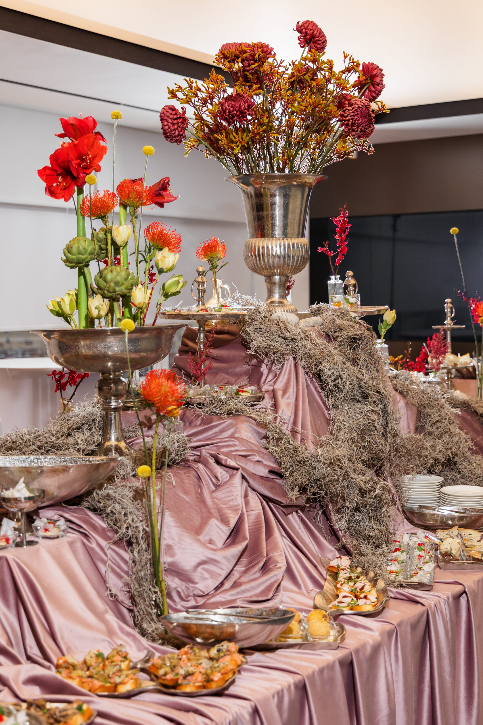 Фуршетный стол с красными цветами и серебряными вазами — флористика и подача Smile Event Catering
