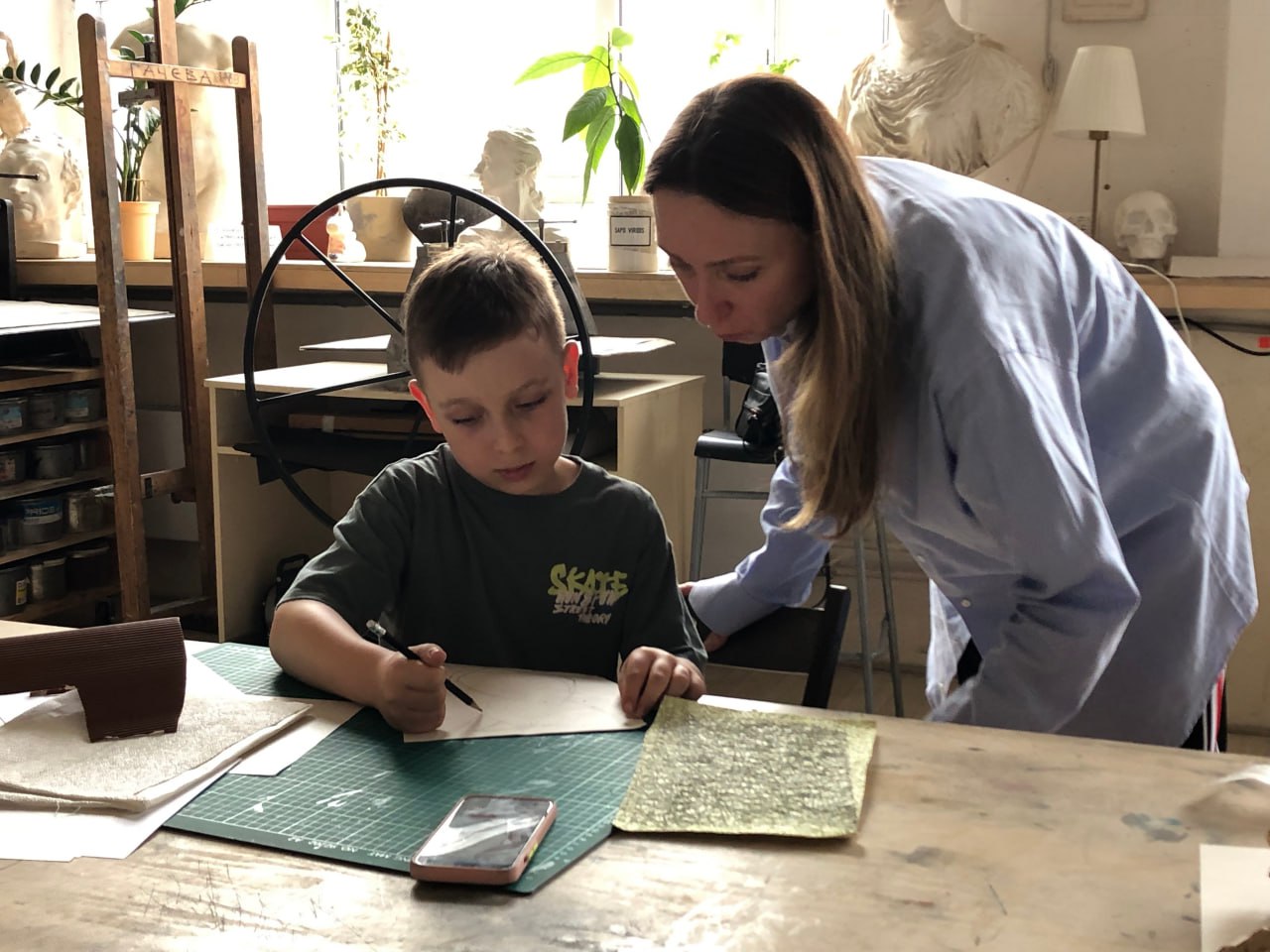 Женщина и мальчик вместе работают над художественным или ремесленным проектом за столом в светлой студии.