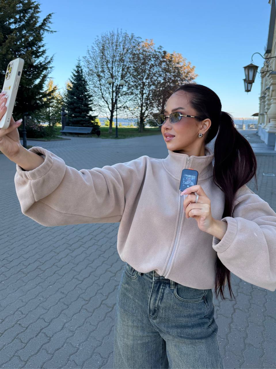 Девушка в бежевой флиске снимает селфи на улице