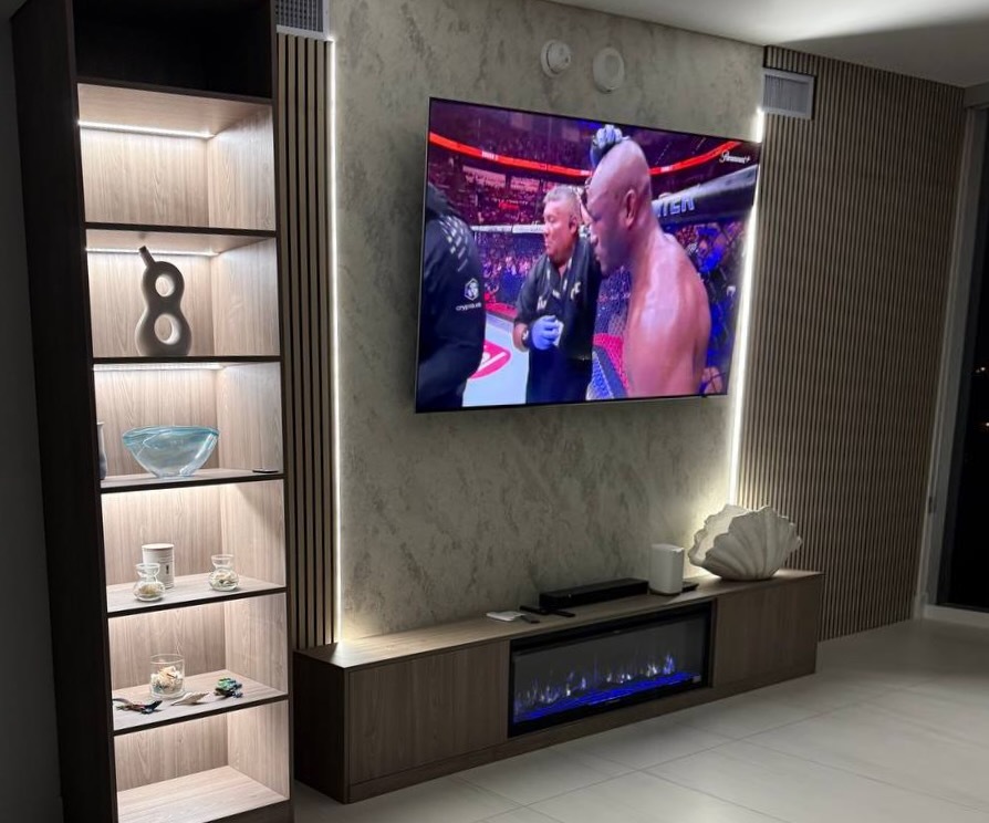 Custom modern media wall in a Miami high-rise featuring a textured plaster finish, integrated LED lighting, floating wood cabinets, illuminated display shelving, vertical wood slats, and a slim linear electric fireplace.