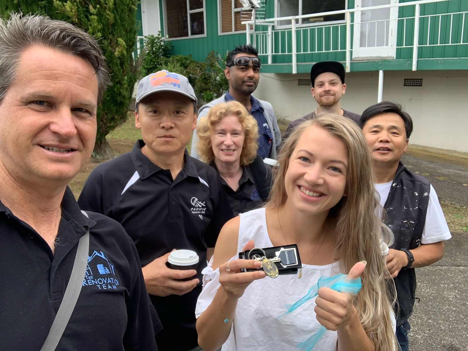 Smiling woman holding house keys with a renovation team standing outside a green house