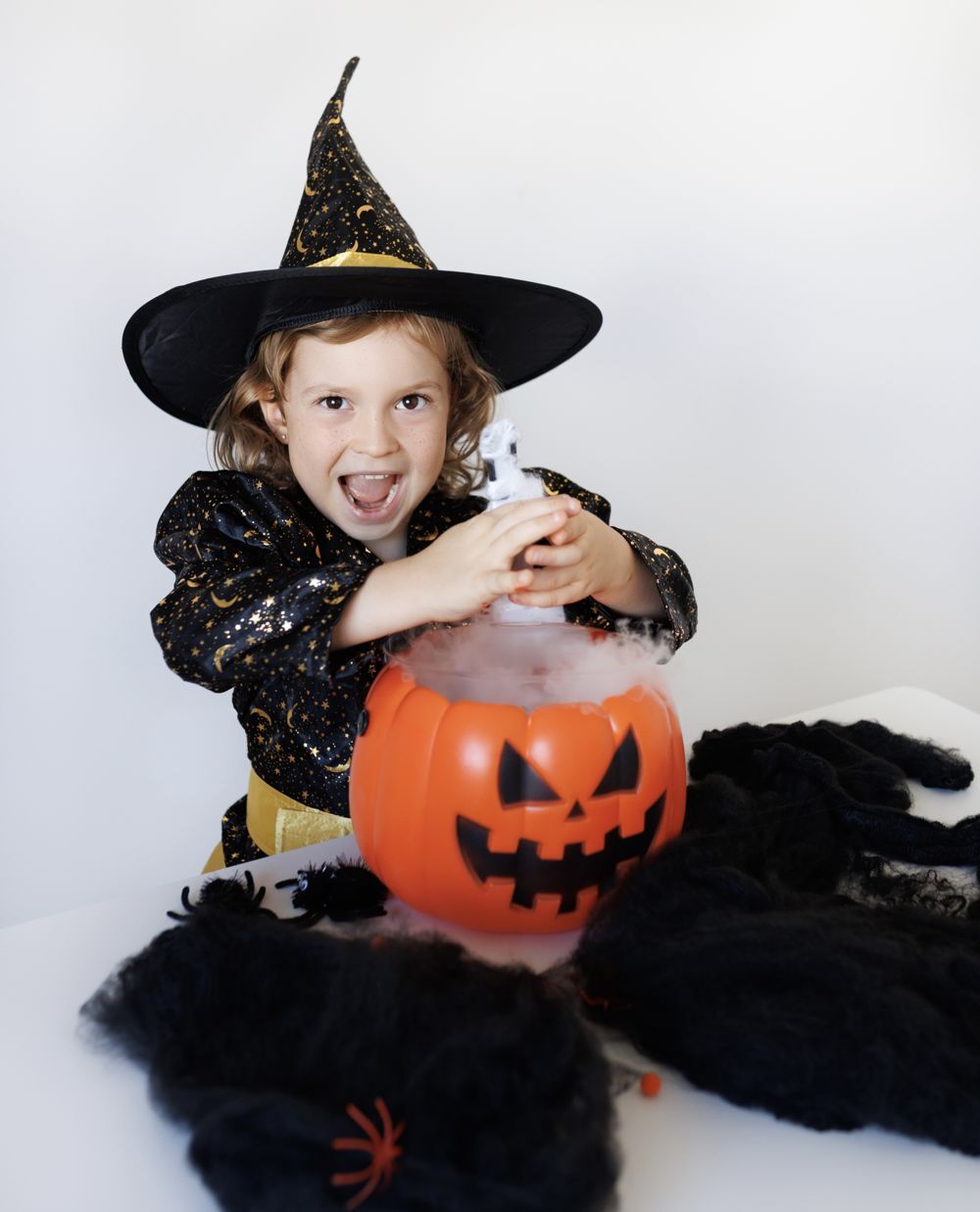 Una niña disfrazada de bruja removiendo un caldero-calabaza humeante