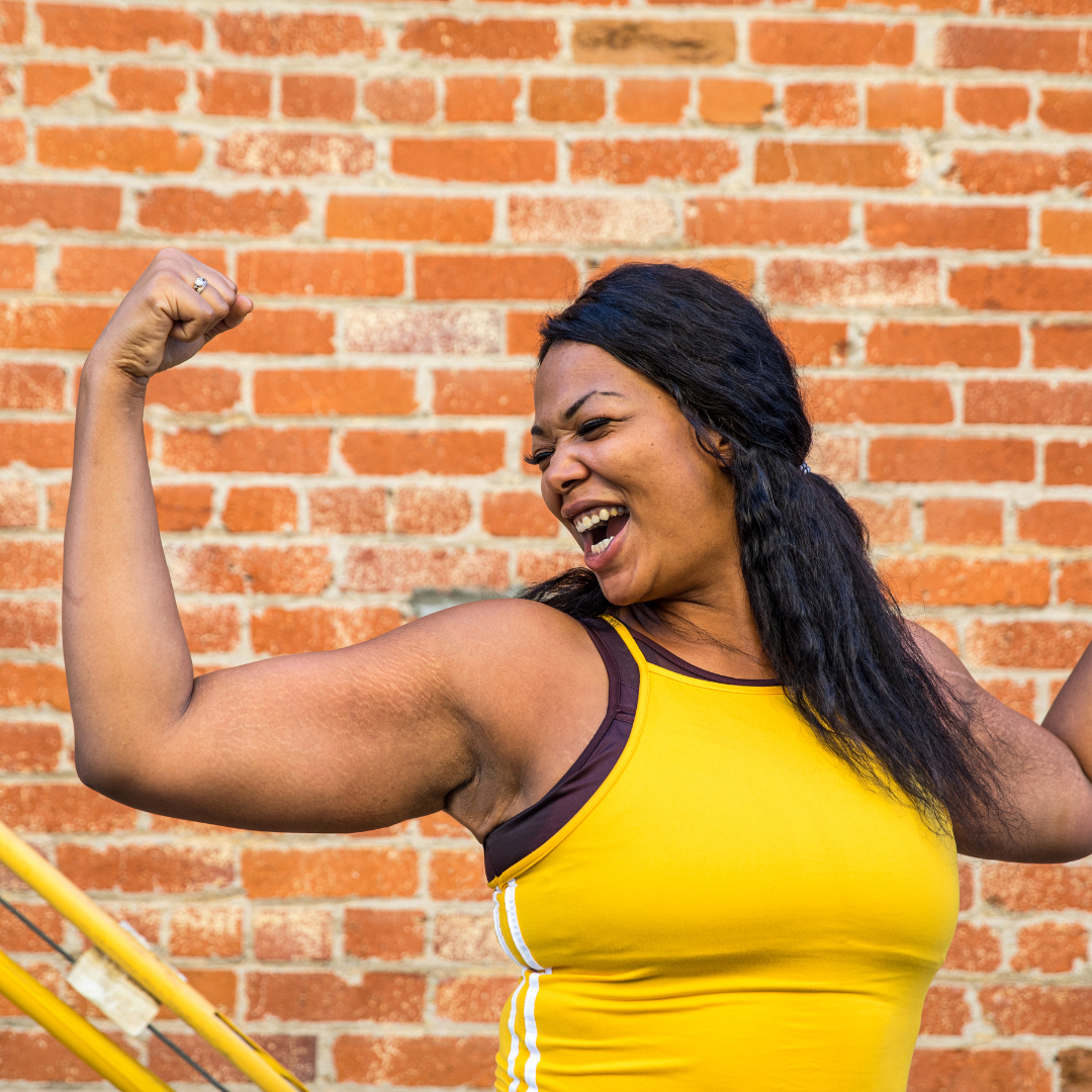 a black woman with their arms up in front of a brick wall