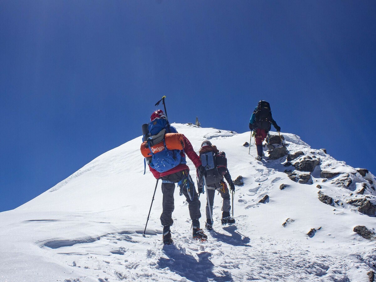 Two roped climbers with packs approaching a snowy summit ridge under a deep blue sky