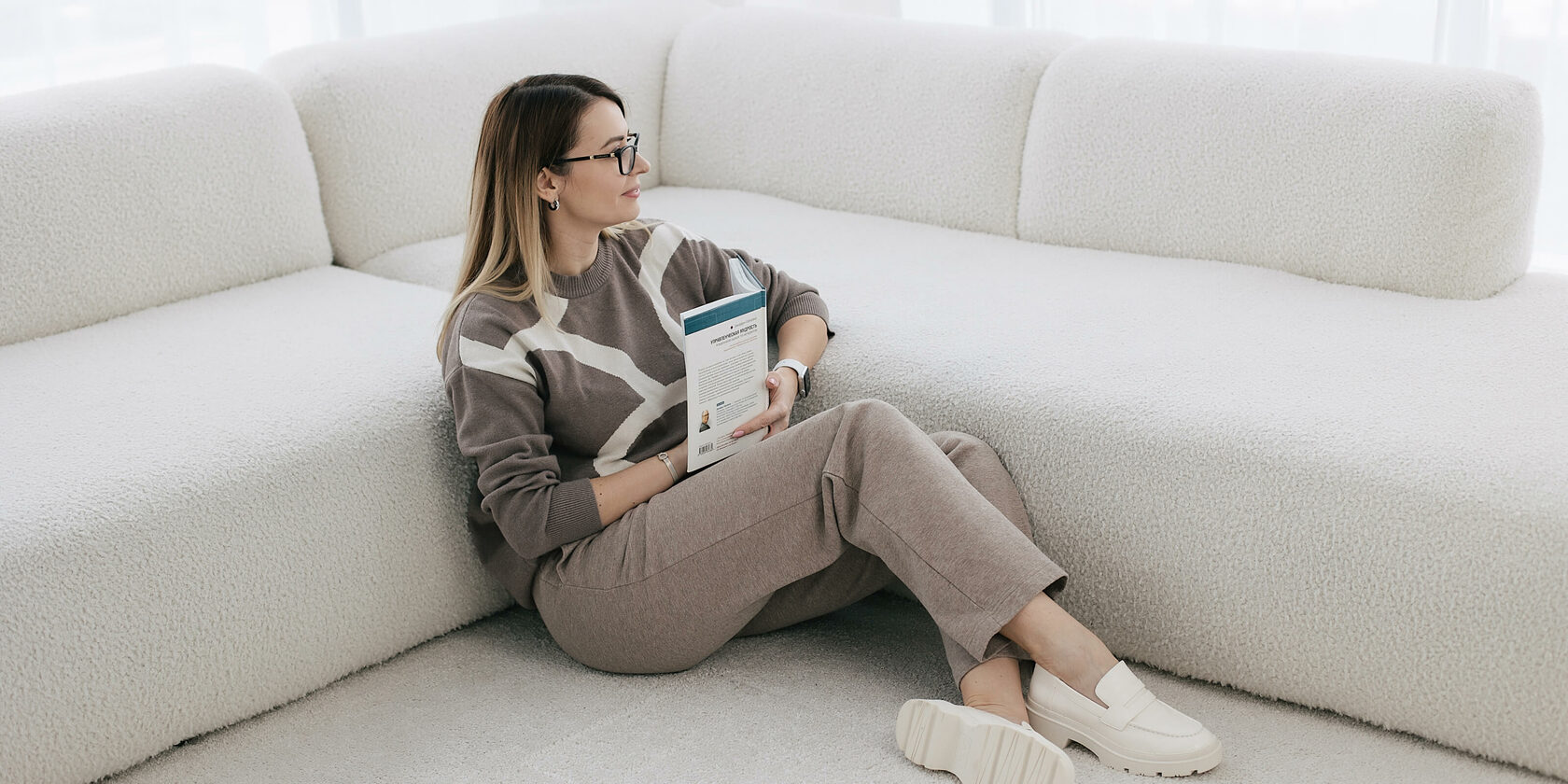 Профессиональный стилист и имиджмейкер улыбается и сидит на полу с книгой в руках