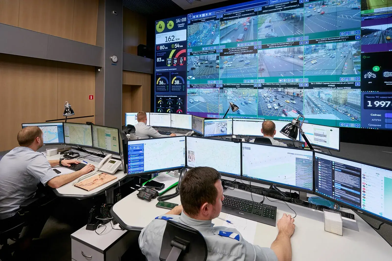 Операторы в форме работают за компьютерами в современном ситуационном центре МВД с большими экранами на стене.