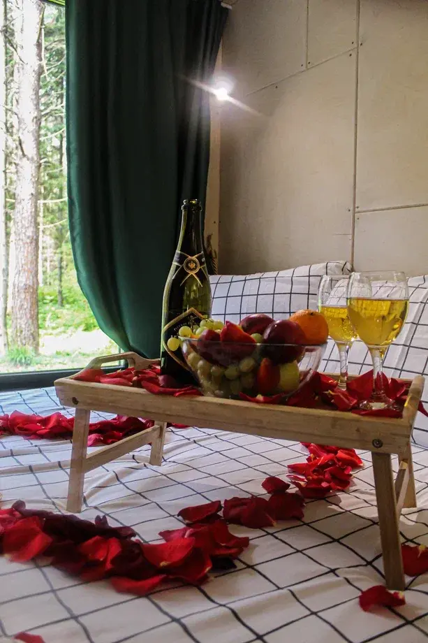 Romantic Home в глэмпинге Тишина: поднос с фруктами, шампанским и лепестками роз на кровати — романтическое оформление домика для пары в сосновом лесу