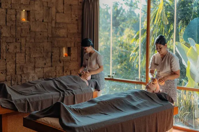 Two therapists performing a calming facial treatment on a couple at Svaha Spa, highlighting the lush jungle valley views that make it a top contender for the best spa in Ubud.