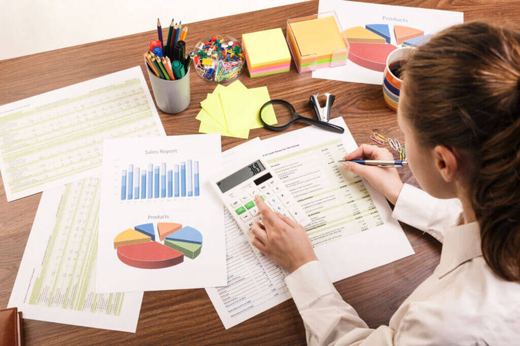 A female accountant is calculating on a calculator at a desk surrounded by stationery items.