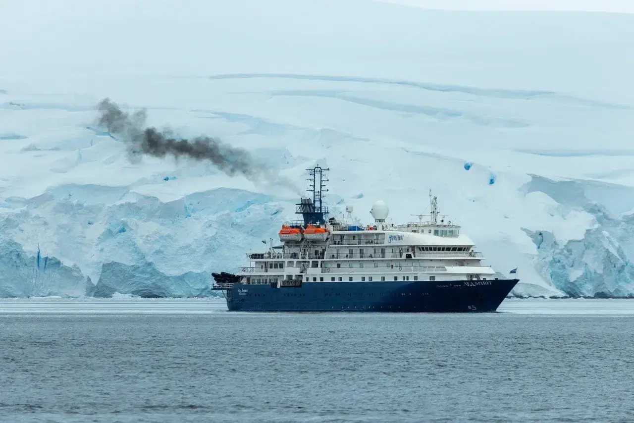 Large expedition cruise ship operating in Antarctica with engine emissions visible against Antarctic glaciers.