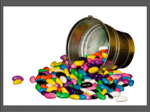 Металлическое ведро, из которого рассыпались разноцветные конфеты-бобы на белом фоне.