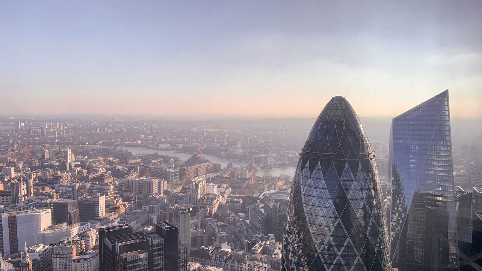 The City of London from above at low sun, with the Gherkin and the Scalpel towers in front and the Thames and Tower Bridge behind