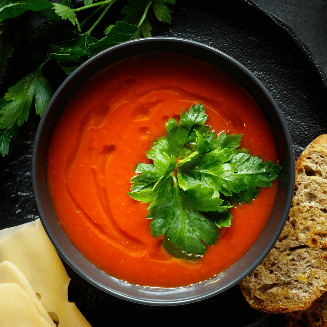 Kalte Tomatensuppe in schwarzer Suppenschüssel mit Kräutern garniert