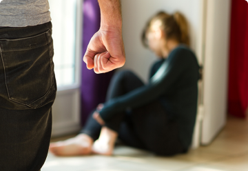 женщина испуганно сидит в углу, мужчина с кулаком