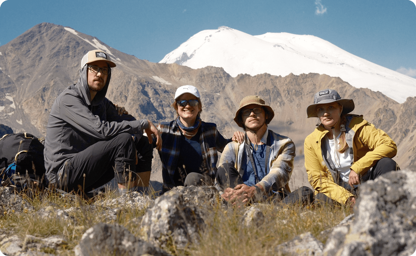 Группа из четырех друзей на фоне заснеженной вершины горы Эльбрус в солнечный день во время похода