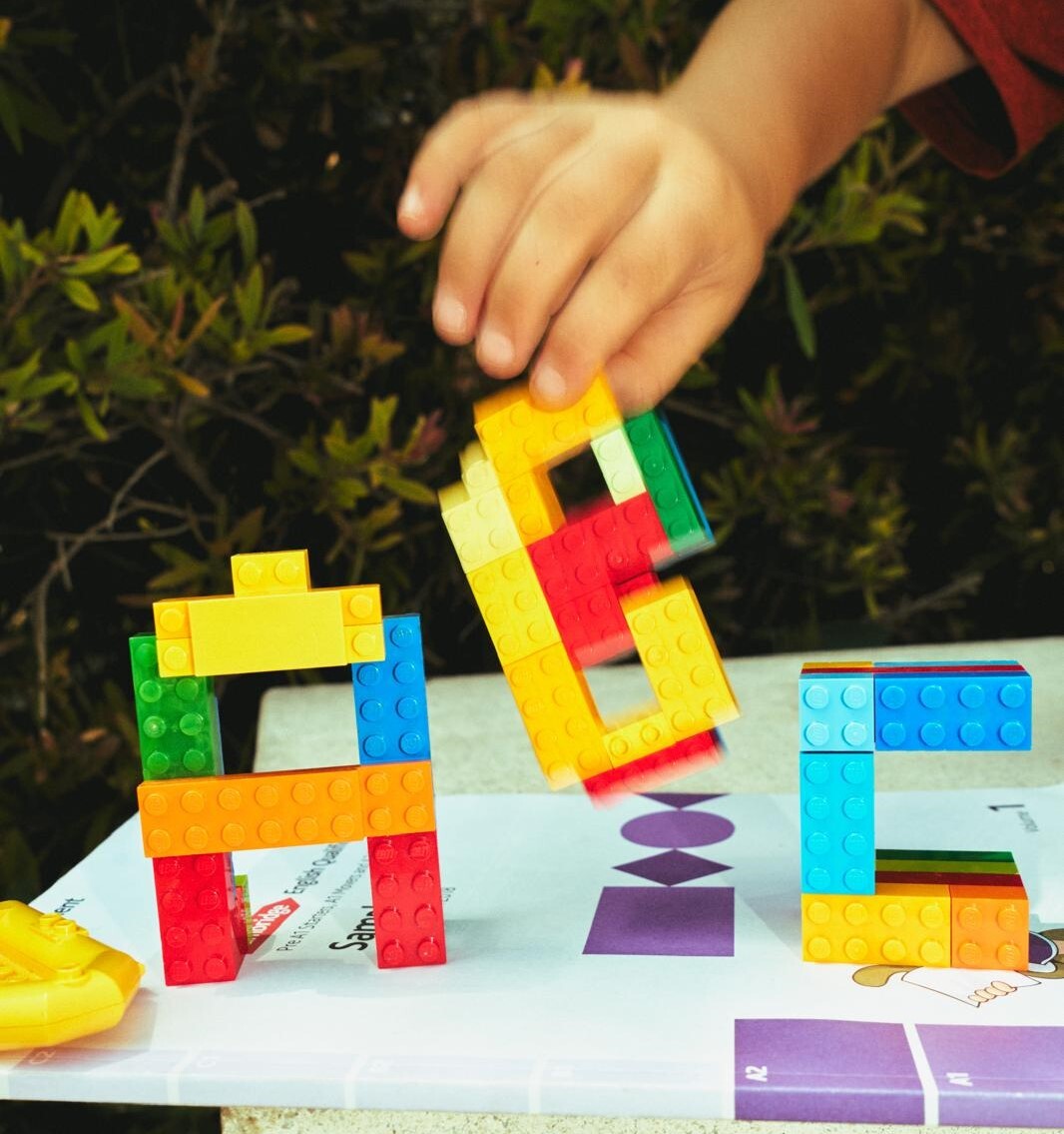 Niño jugando con bloques de construcción de colores formando letras sobre un cuaderno