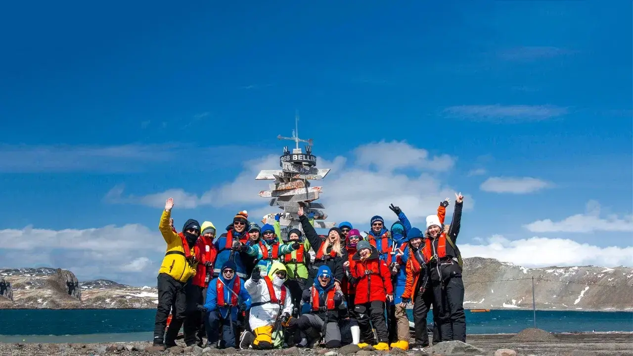 Participants of the MoreTime Expeditions Antarctic Science Camp gathered on King George Island near Bellingshausen Station. The group celebrates at a famous directional signpost after a week of scientific activities exploration and unforgettable adventure