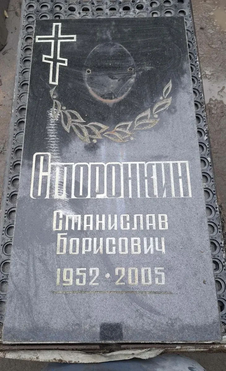 Тёмная стела до обновления: надпись, крест, овальный след от фотографии и растительный орнамент.
