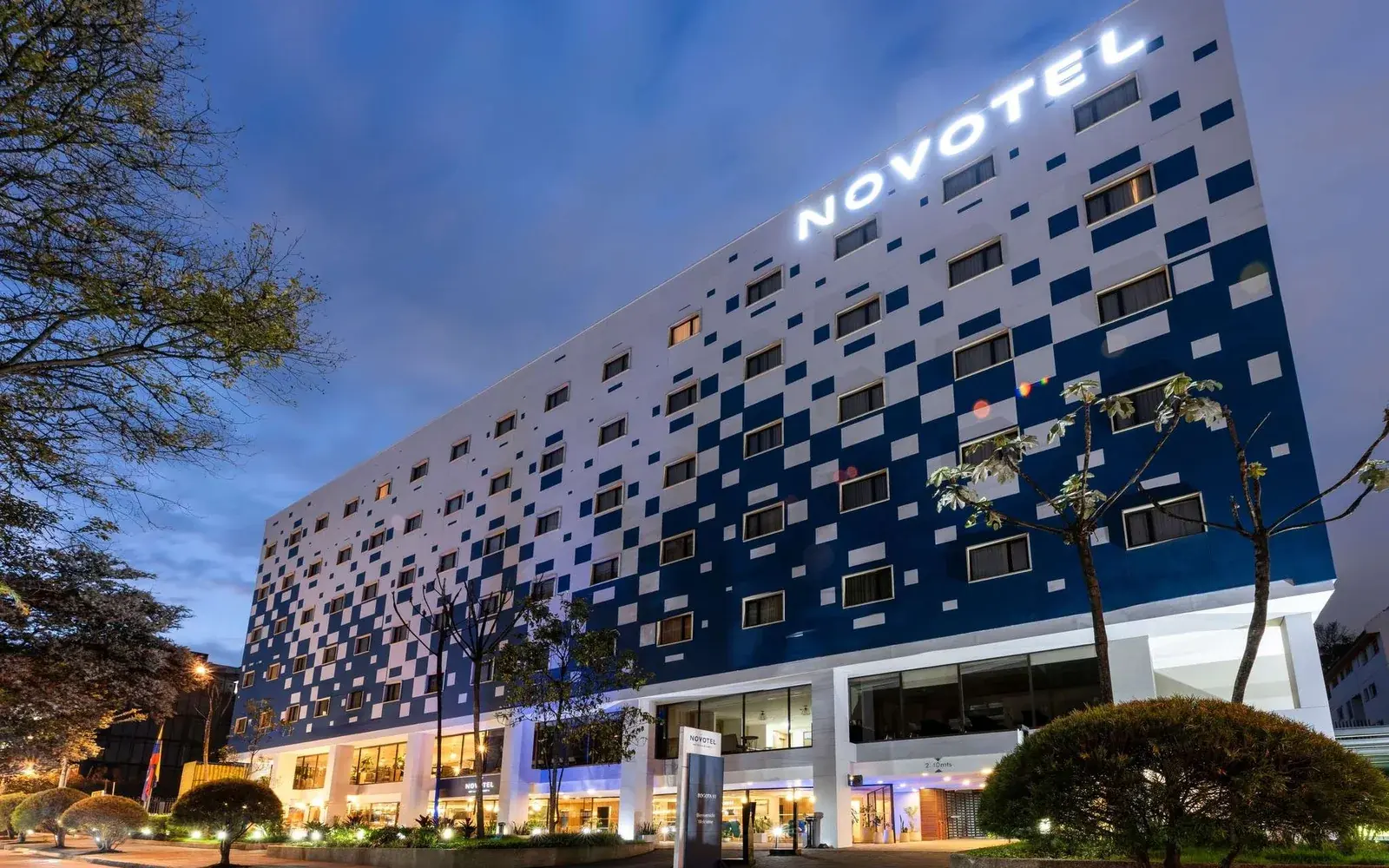 Фасад Novotel Bogota Parque 93 в сумерках с подсвеченной вывеской, Богота