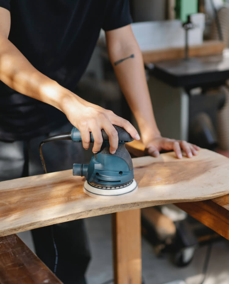 Ein Handwerker schleift eine Holzplatte mit einem Schleifer