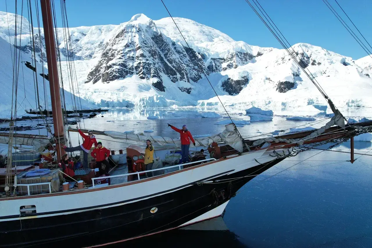 Small group aboard an expedition sailing yacht exploring Antarctica surrounded by glaciers and snow-covered mountains