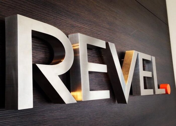 Буквы REVEL крупным планом: металлическое лицо и глубокий борт на деревянной стене