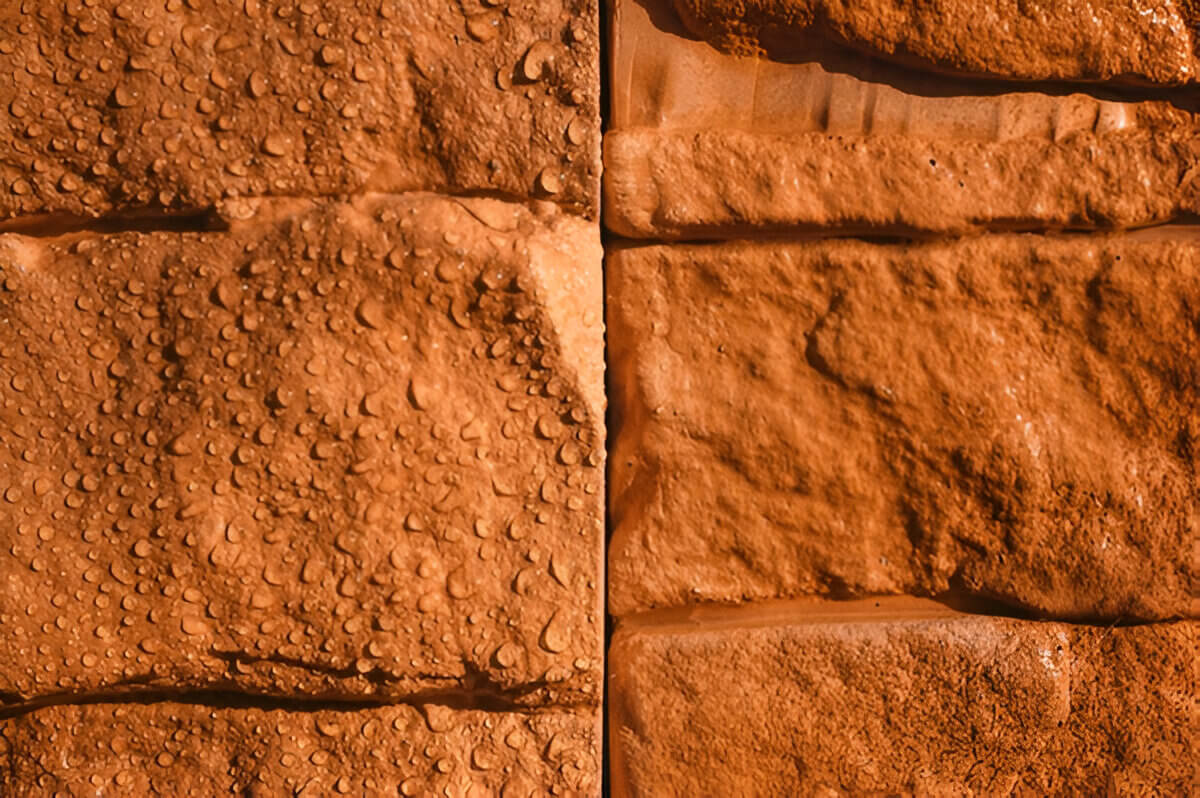 Каменная облицовка крупным планом. Слева поверхность после гидрофобизации с водяными каплями, справа тот же материал без защиты, вода впитывается. Иллюстрация разницы в водоотталкивании.