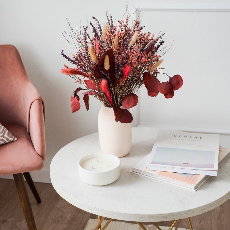 букет из красных сухоцветов в глиняной вазе в интерьере со свечей и журналами
