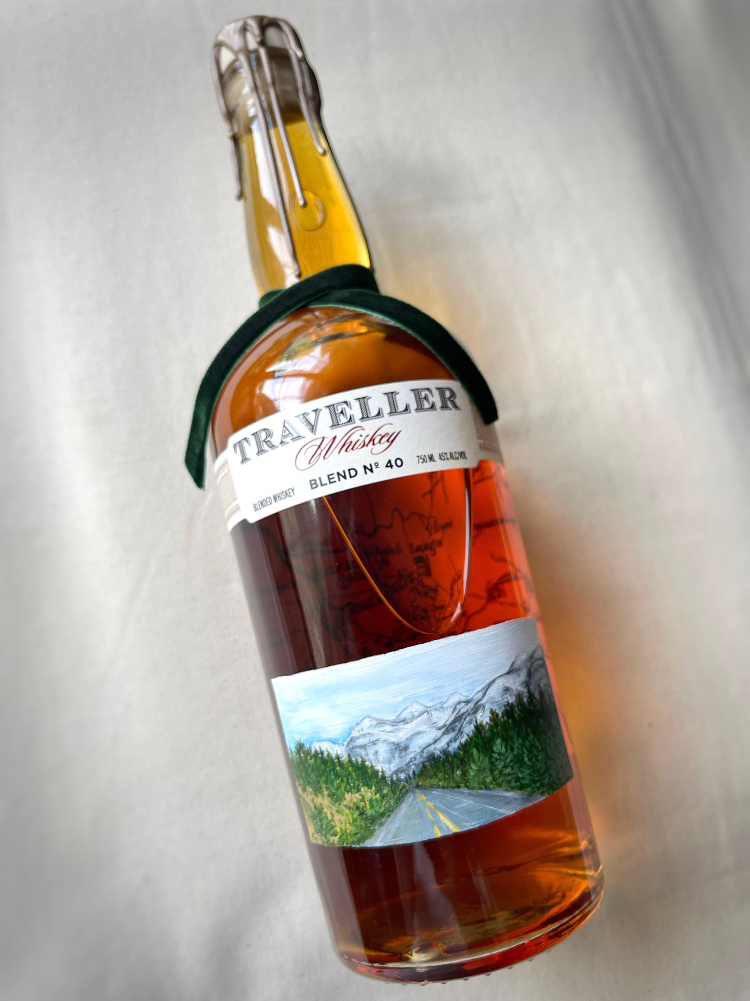 Hand-painted Traveller Whiskey bottle featuring a detailed mountain road landscape artwork by Julia Razz.