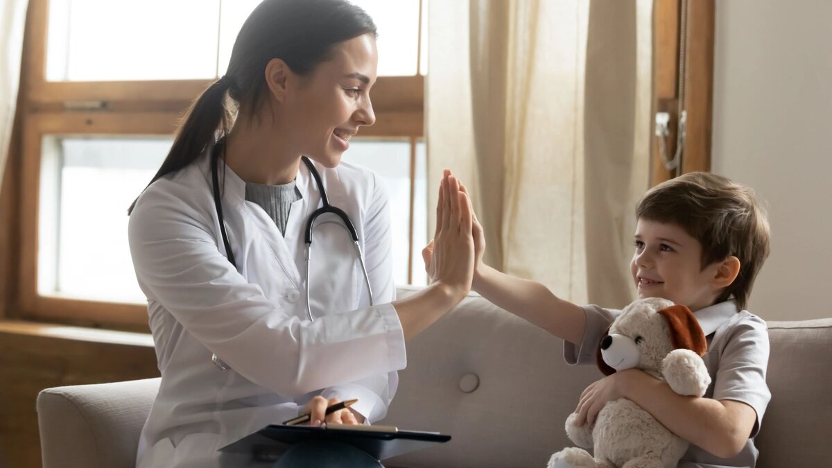 Улыбающийся детский врач дает пять маленькому мальчику в кабинете, иллюстрация позитивного празднования Дня педиатра.