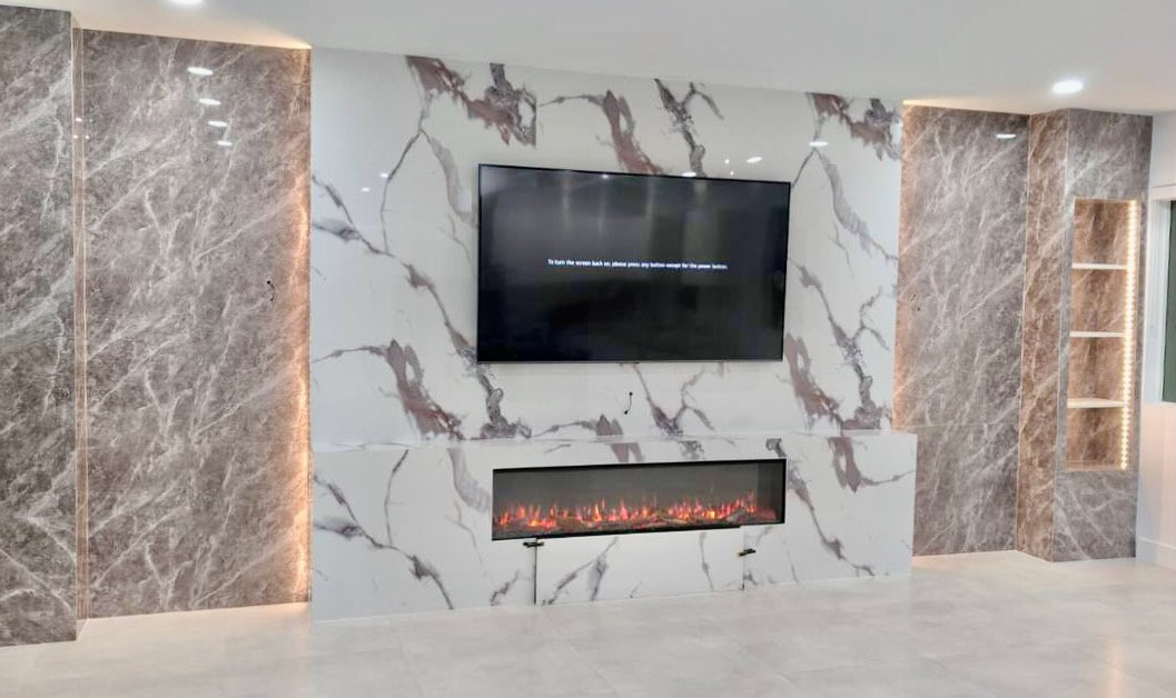 Full view of a contemporary TV and fireplace wall with contrasting marble-look panels, architectural columns, and illuminated display niches.
