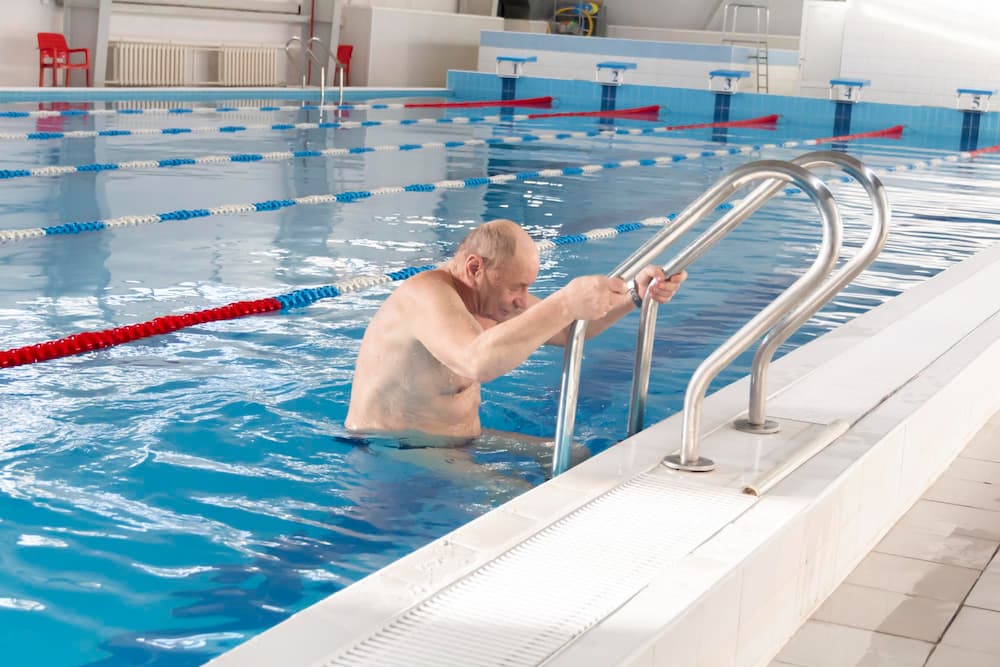 Взрослый привыкает к воде у бортика бассейна
