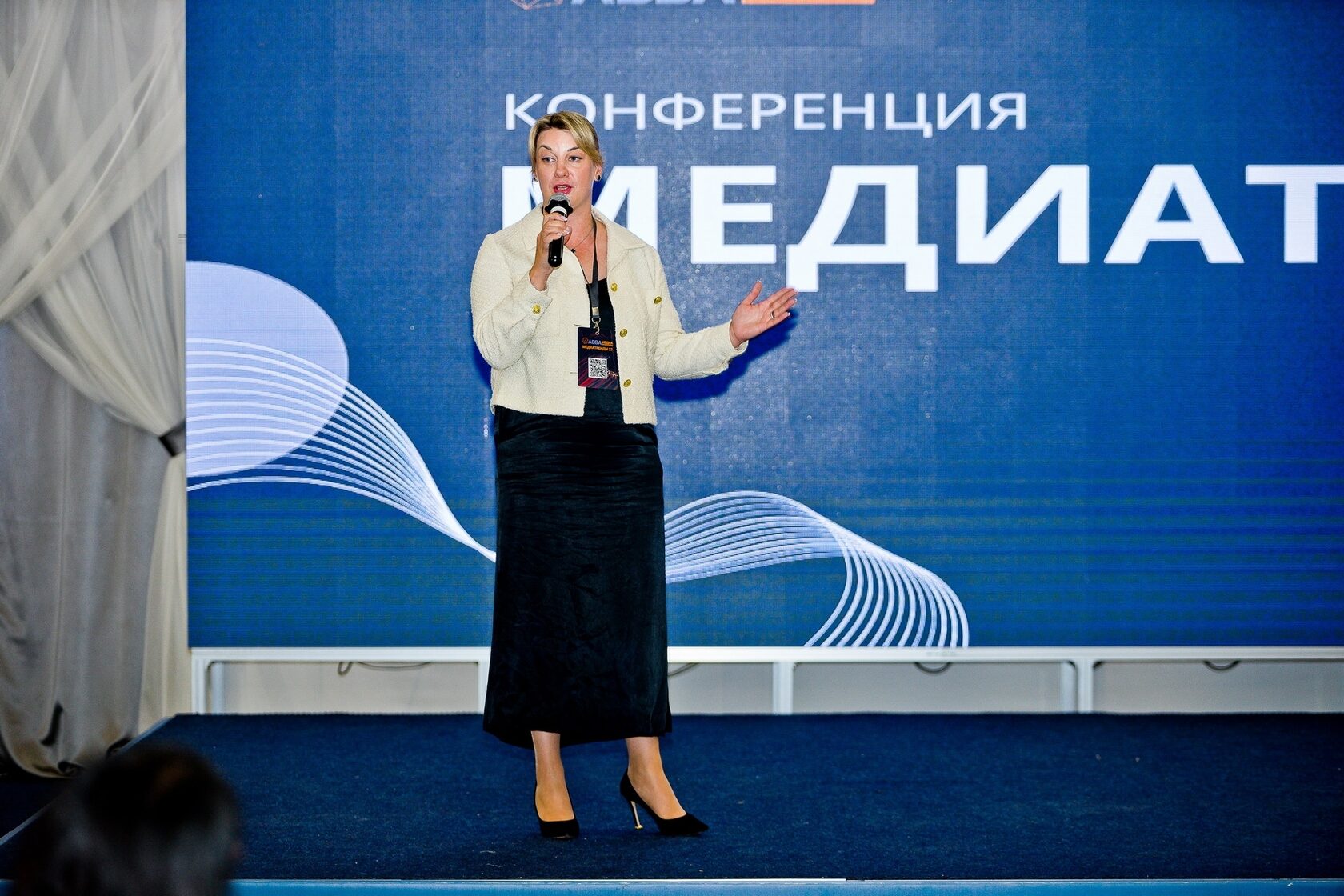 Спикер на сцене с микрофоном на фоне экрана «Медиатренды»