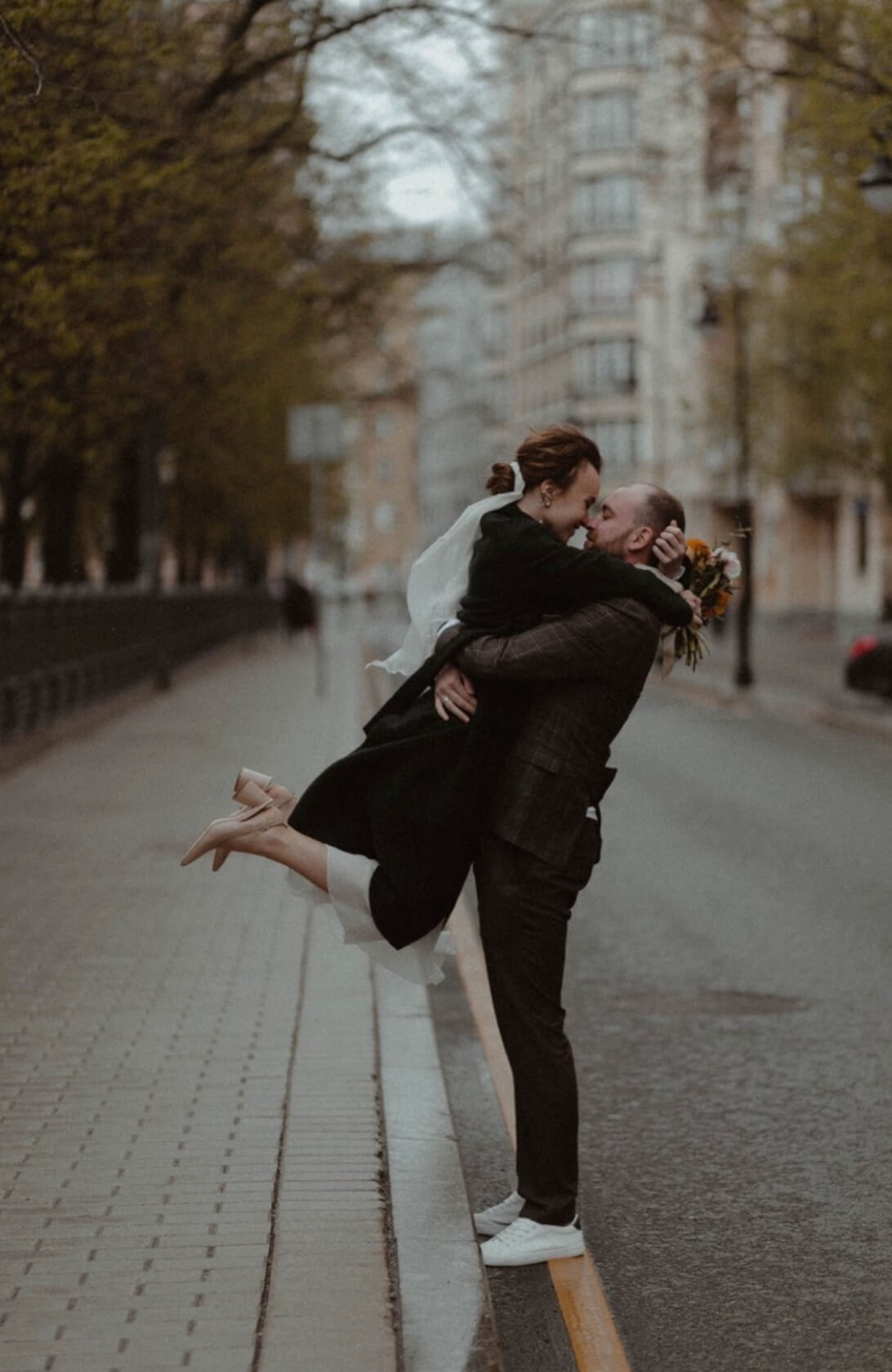 Невесту держит жених на руках во время дождя