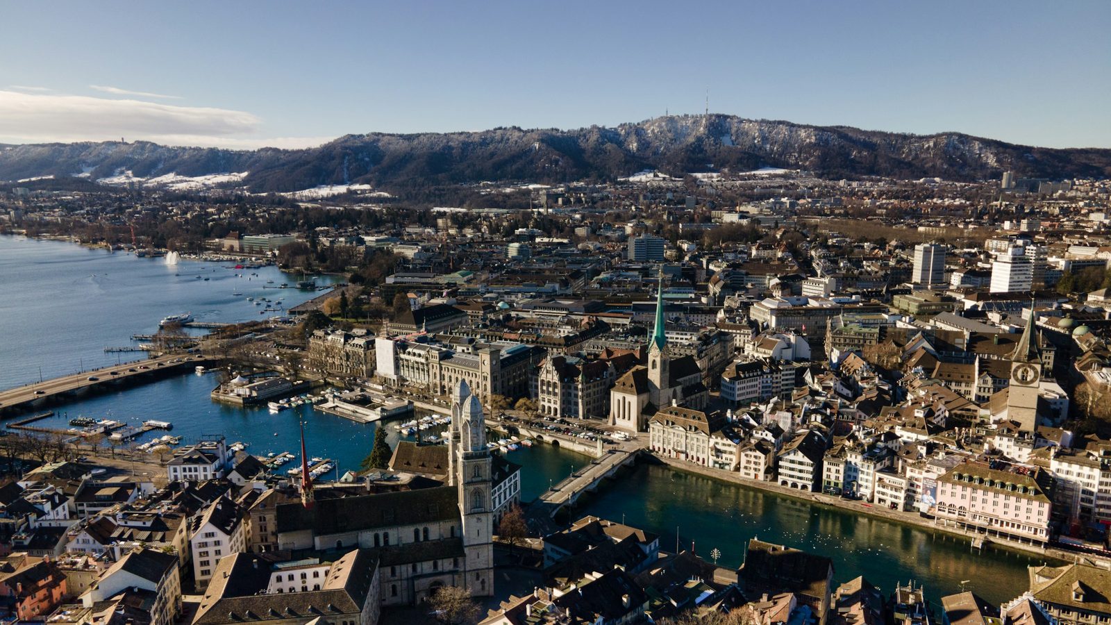 Aerial view of Zurich's old town on a clear winter day, with the twin towers of the Grossmünster, the Limmat river, Lake Zurich and the snowy Uetliberg behind