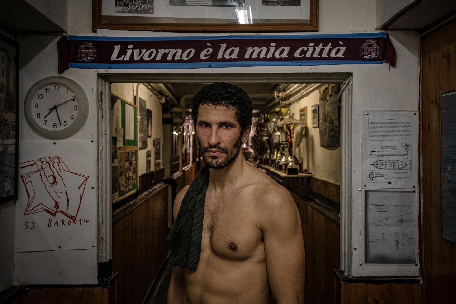 Italy | Michele Martinelli. Karim Rashedi, a rower from the historic Borgo Cappuccini district, stands at the entrance of his local rowing club in Livorno.