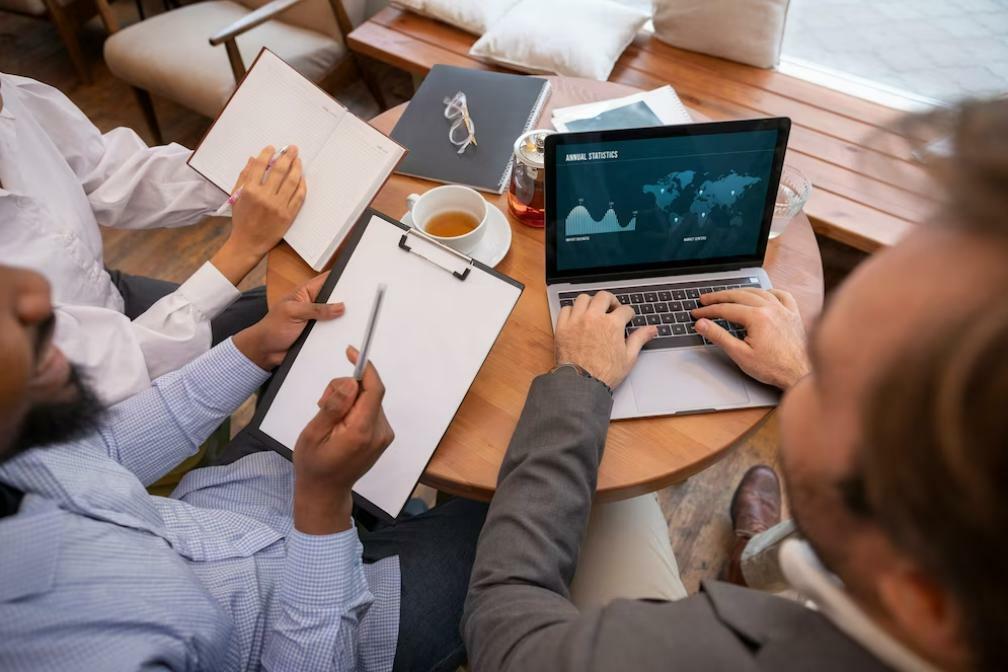 Tres personas junto a una mesa analizando el análisis técnico de un cuaderno y una computadora portátil