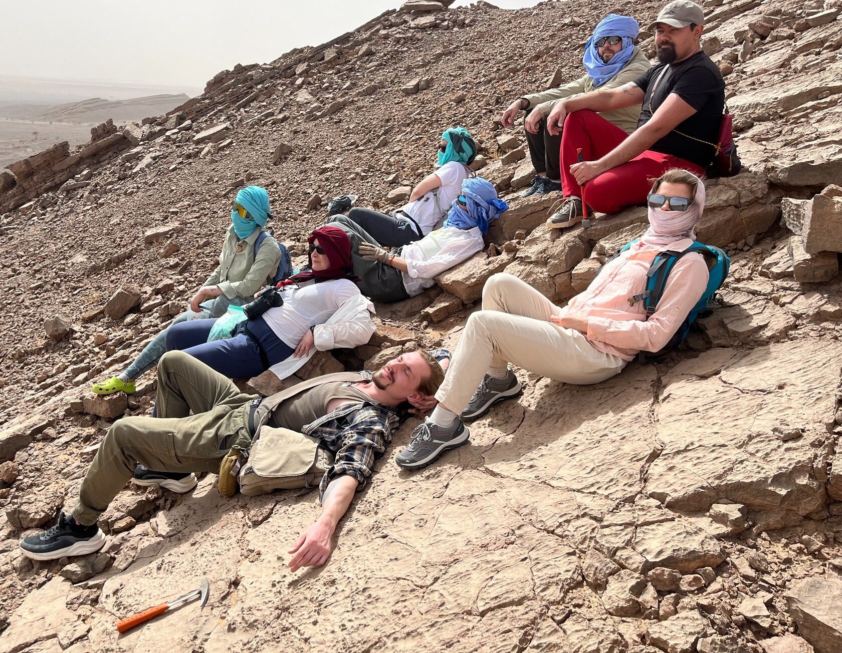group of fossil hunters resting on rocky slope during Sahara desert expedition