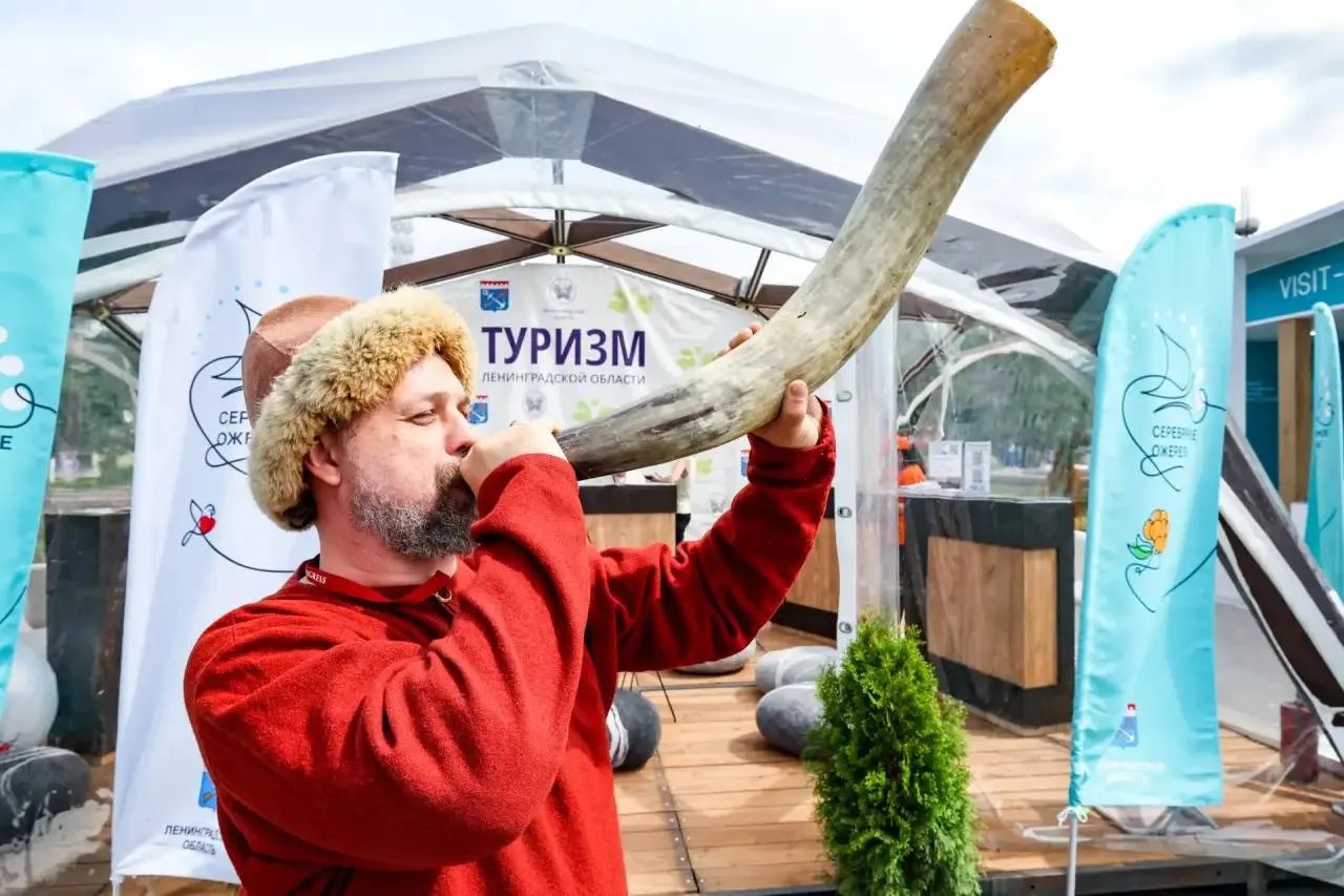 Мужчина в традиционной одежде играет на роге на стенде туризма Ленинградской области на форуме «Путешествуй!» на ВДНХ в Москве.