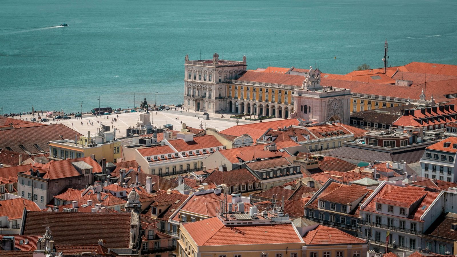 Praça do Comércio in Lisbon seen from above, with the Rua Augusta Arch, yellow arcaded buildings, red roofs and the Tagus river behind