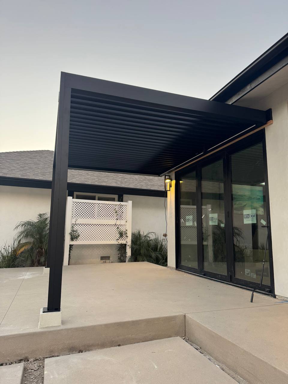 Close view of the completed louvered pergola roof, front post and concrete patio.