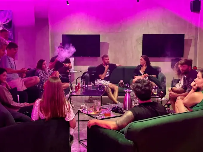 A large group of friends gathering for a relaxed evening of hookah under atmospheric pink lighting at Hookah Mansion, a spacious option for the best shisha lounge in Bali.