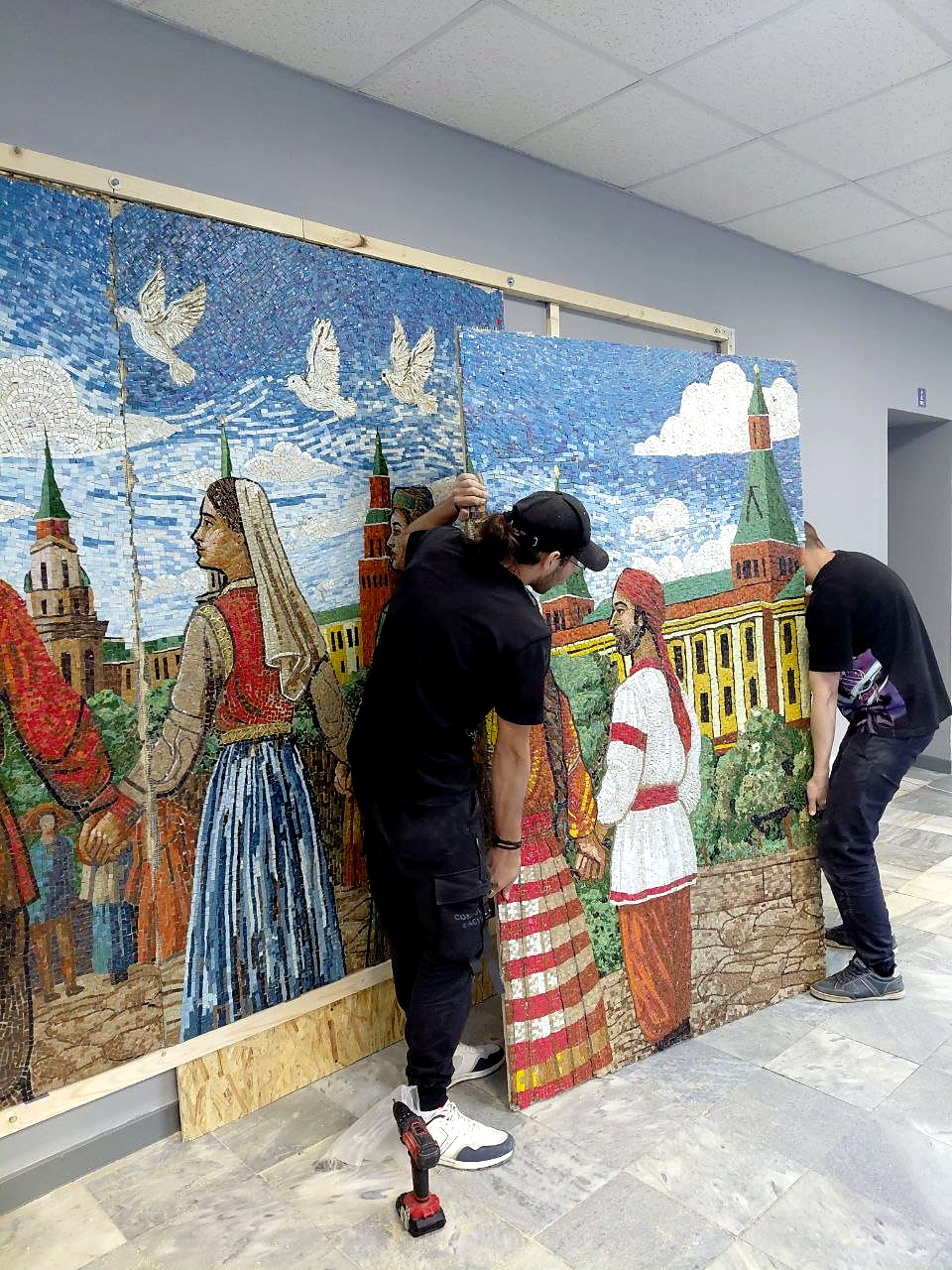Мастер ArtWorker крепит мозаичное панно к деревянному каркасу на стене РУДН