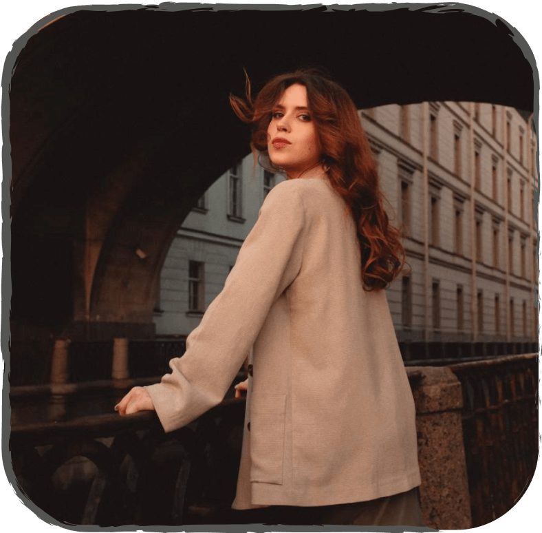 девушка шатенка в бежевом пиджаке смотрит в камеру на фоне мост Санкт-Петербург