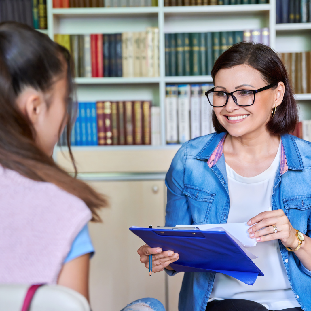 a person is talking to a person in front of a bookshelf