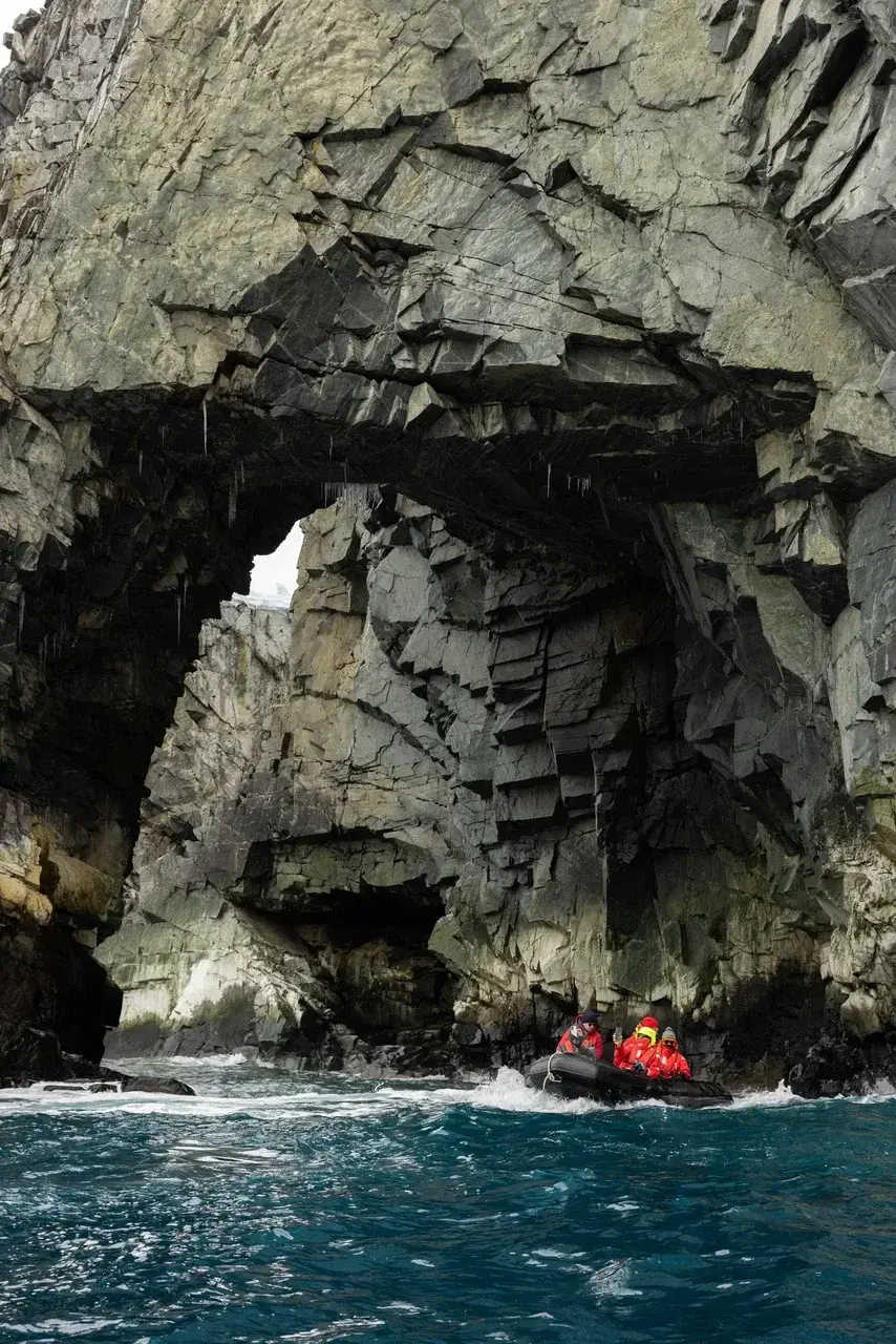 Zodiac expedition boat exploring dramatic rocky cliffs and sea caves in Antarctica during a small-group Antarctic adventure