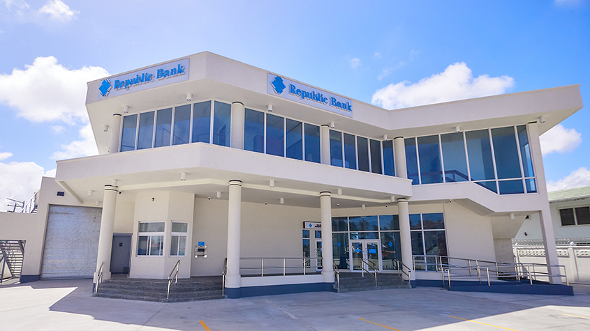 A two-story, modern building with a clean, white facade and large windows. The building has signs for Republic Bank in blue lettering. The entrance is marked by a set of steps leading to glass doors, and a small, covered area with a ramp and ATM is visibl