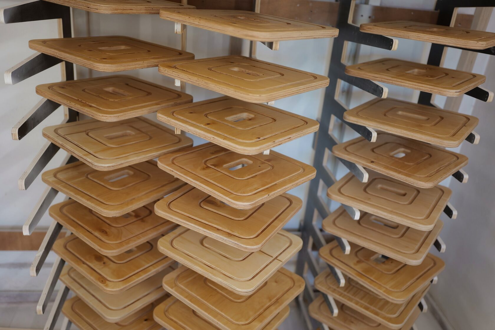 Identical plywood seat tops stacked on a drying rack